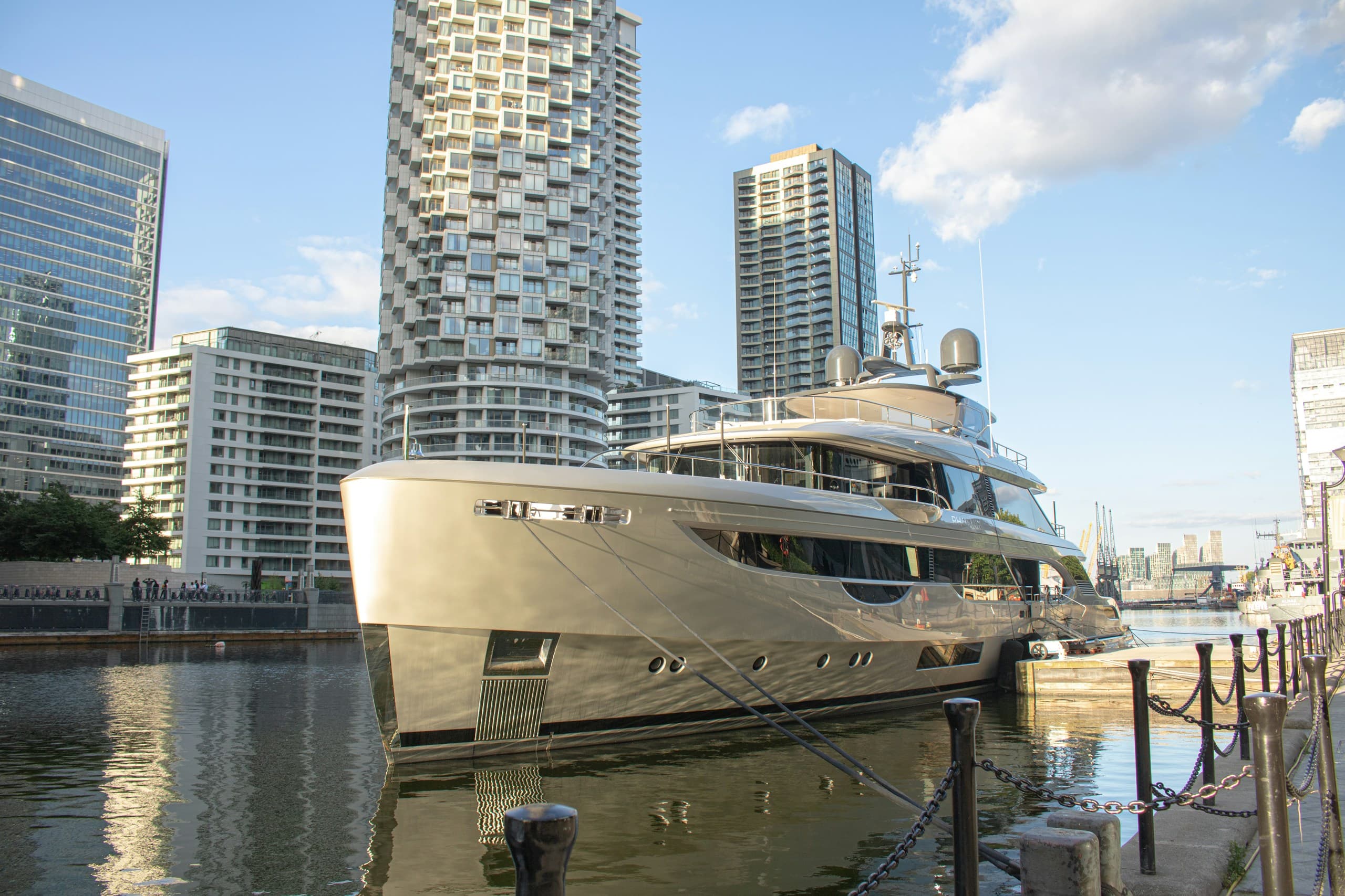 A motor yacht lying alongside in West India Dock, with the Canary Wharf towers beyond